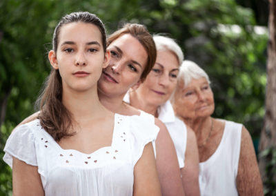 Portrait von einer Familie. Vier Frauen verschiedener Generationen in weißer Kleidung. Stehen hintereinander nach dem Alter geordnet. Im Hintergrund Bäume.