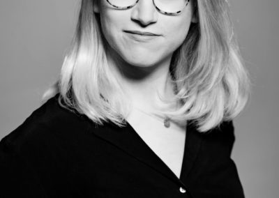 Schwarzweiß-Portrait einer jungen Frau mit Brille und halblangen blonden Haaren.