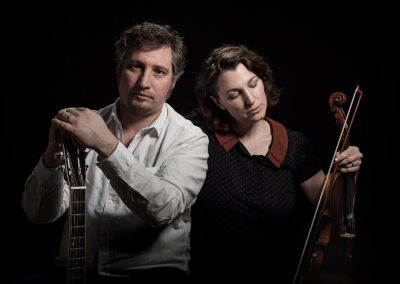 Portrait eines musikalischen Ehepaars. Frau mit Violine und Mann mit Gitarre. Hintergrund schwarz.